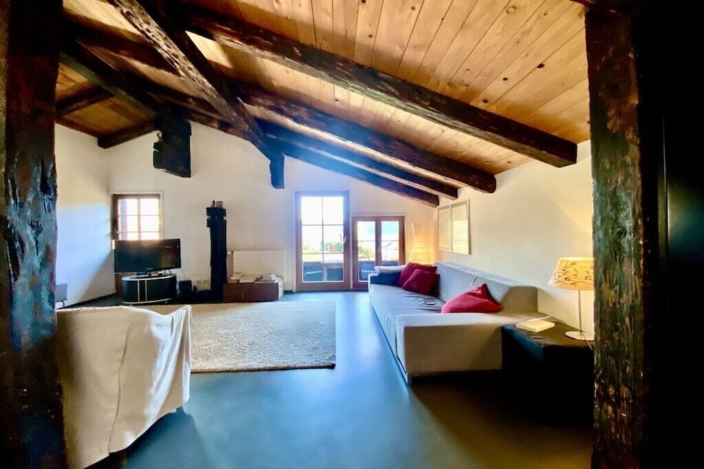 A room with a high ceiling, wooden beams, a sofa set, a television, and a fireplace.
