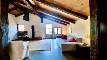 A room with a high ceiling, wooden beams, a sofa set, a television, and a fireplace.