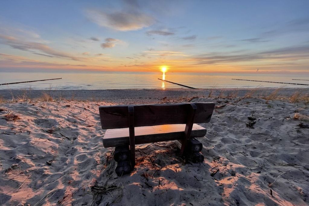 Un banc sur une plage de sable, avec un coucher de soleil en arrière-plan.