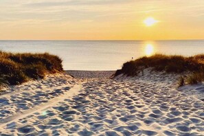 A sandy beach path leading to the sea with a sunset in the background.
