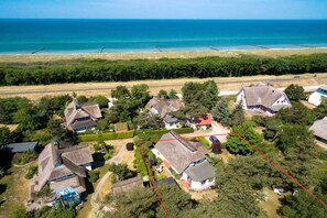 An aerial view of a residential area with houses, a beach, and a clear sky.