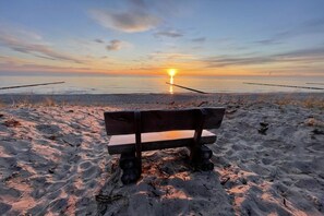 A bench on a sandy beach with a sunset in the background. - Holiday home with 3 bedrooms (Ostseebad Wustrow)