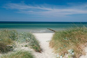 A sandy beach path leading to the ocean with a wooden jetty in the distance.