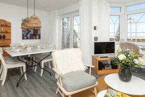 A modern living room with a dining area, a television, and a large window. - Holiday apartment in Juist with swimming pool (Juist)