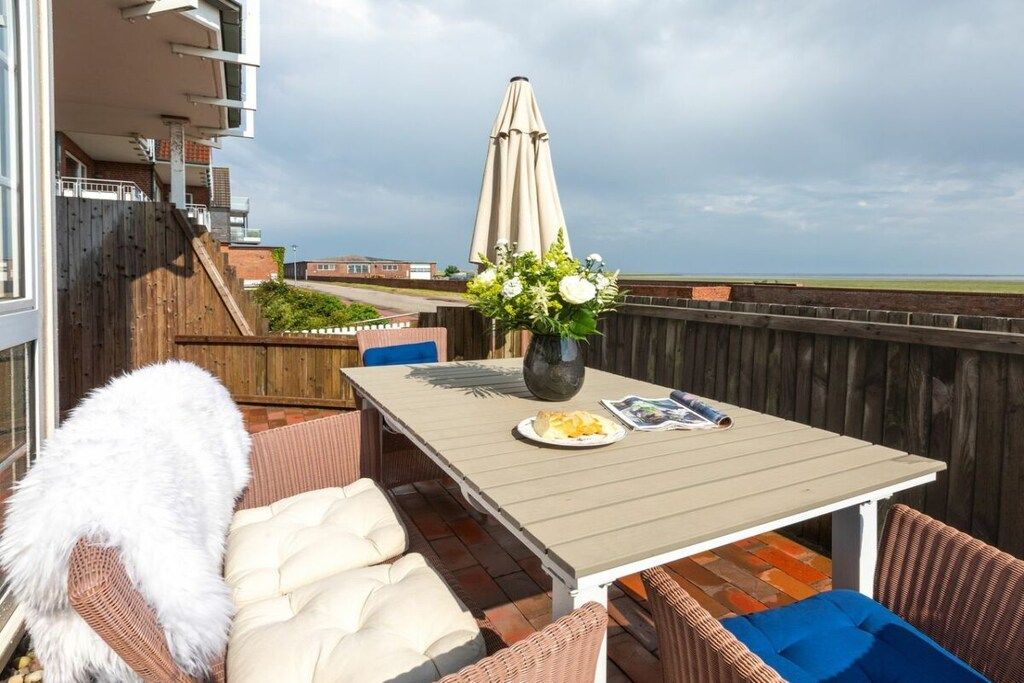 Eine Terrasse im Freien mit Tisch, Stühlen und einer Blumenvase.
