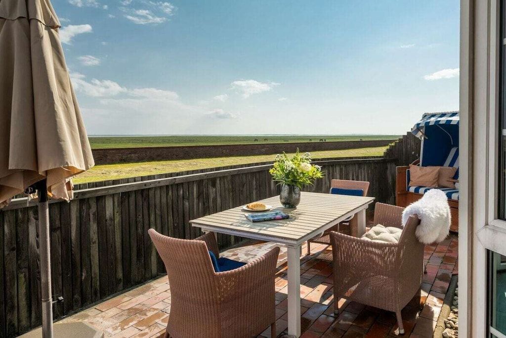 Un patio exterior con una mesa, sillas, una planta en maceta y vistas a la playa.