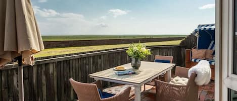 Un patio exterior con una mesa, sillas, una planta en maceta y vistas a la playa.