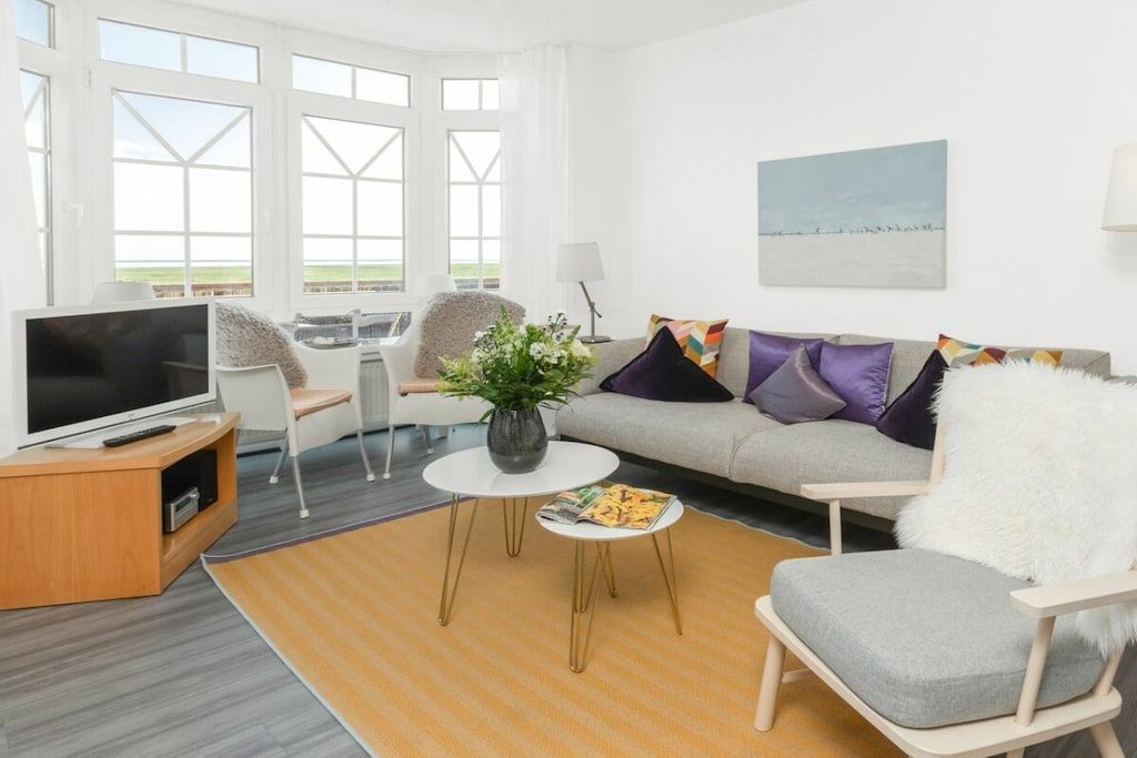Un salon moderne avec un canapé, un fauteuil, un téléviseur et une petite table sur laquelle est posé un vase.