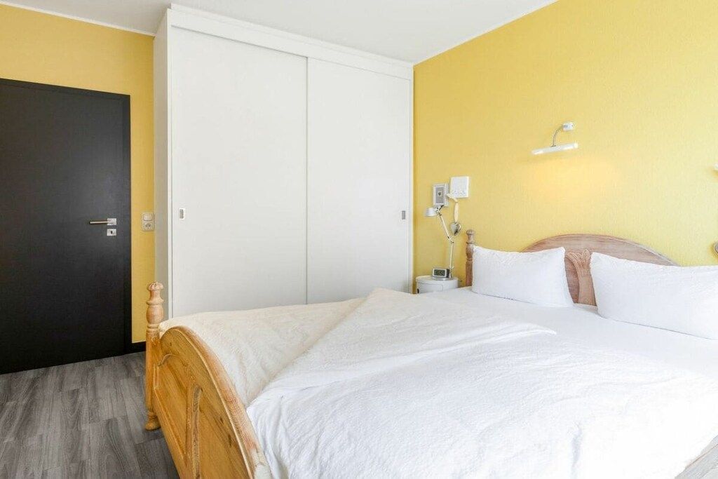Une chambre d’hôtel comprenant un lit, une armoire, une table de chevet avec une lampe et un luminaire fixé au mur.