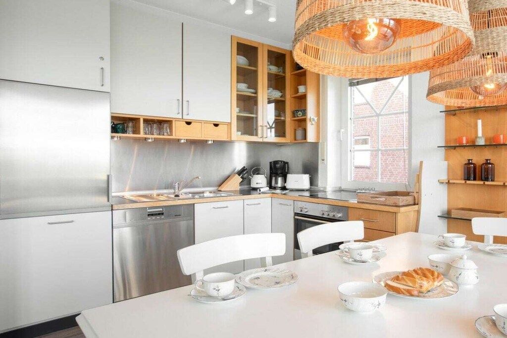 Una cucina moderna con elettrodomestici in acciaio inossidabile, pensili in legno e un'area pranzo con sedie bianche e un tavolo apparecchiato per il tè.