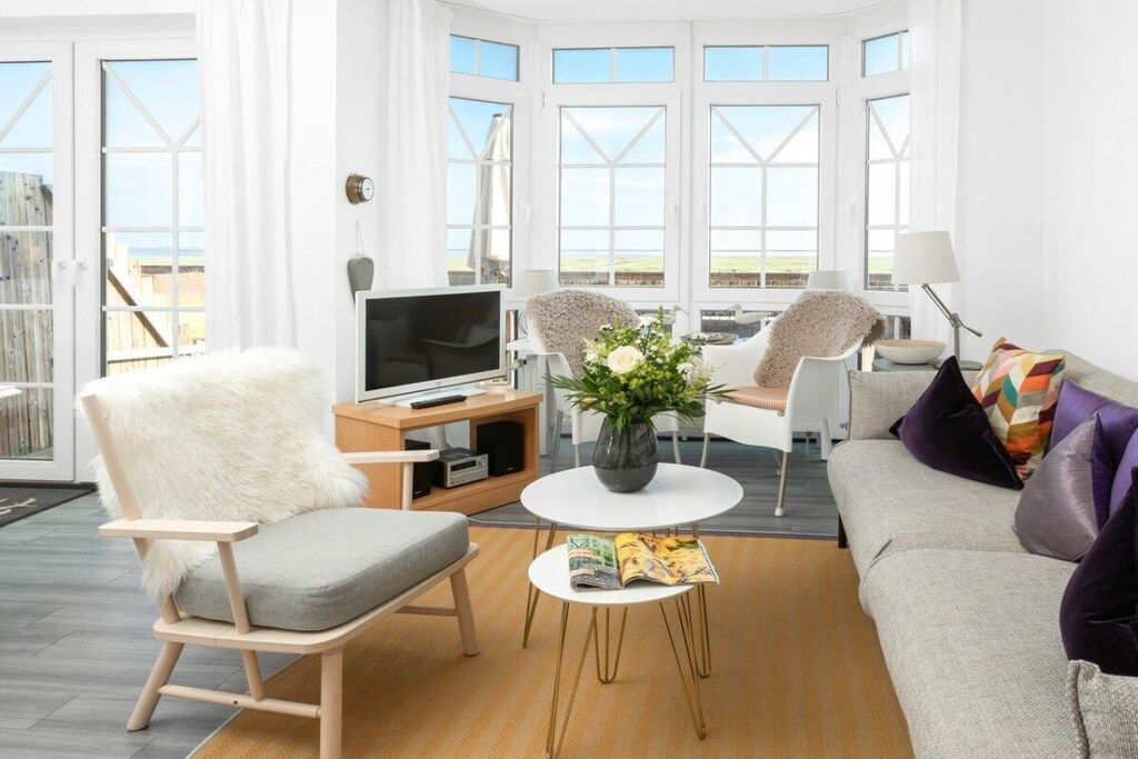 Ein modernes Wohnzimmer mit Sofa, Sesseln, Couchtisch und Fernseher.