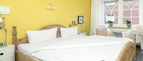 Habitación de hotel con una cama grande, una mesita de noche, una silla, una ventana con vistas a un edificio de ladrillo y una pequeña mesa con una planta.