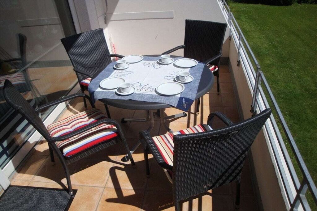 Un balcon avec une table dressée pour quatre personnes, entouré de fauteuils en osier ornés de coussins à rayures.