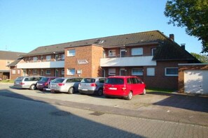 A multi-story building with a parking area in front. - Schütz in the house "Kiebitzwiese" (Borkum)
