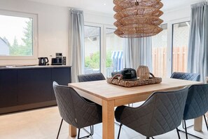 A modern kitchen with a dining area, featuring a wooden table, quilted chairs, and a woven light fixture. - Holiday home with 4 bedrooms (Timmendorfer Strand)