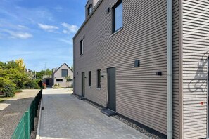A modern building with a flat roof, a paved walkway, and a green fence. - Holiday home with 4 bedrooms (Timmendorfer Strand)