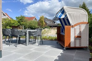 A patio with a table and chairs, a wicker chair, and a small wooden structure. - Holiday home with 4 bedrooms (Timmendorfer Strand)