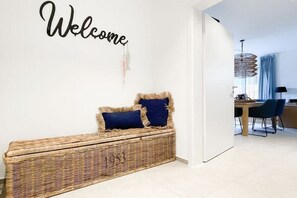 A room with a wicker bench, a wall sign saying 'Welcome', and a glimpse of a dining area in the background. - Holiday home with 4 bedrooms (Timmendorfer Strand)