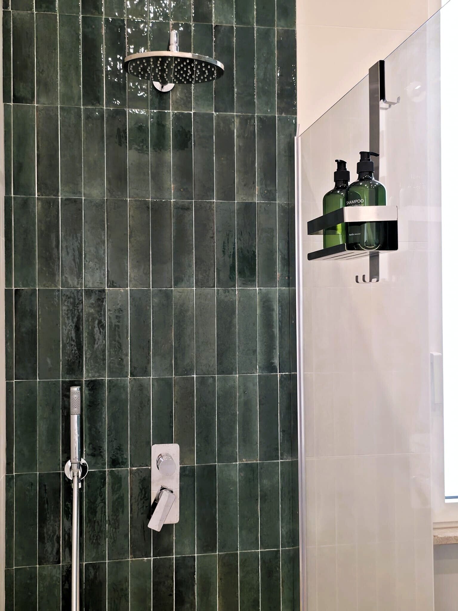 A bathroom with a shower, a hand dryer, and a bottle of shampoo on a shelf.