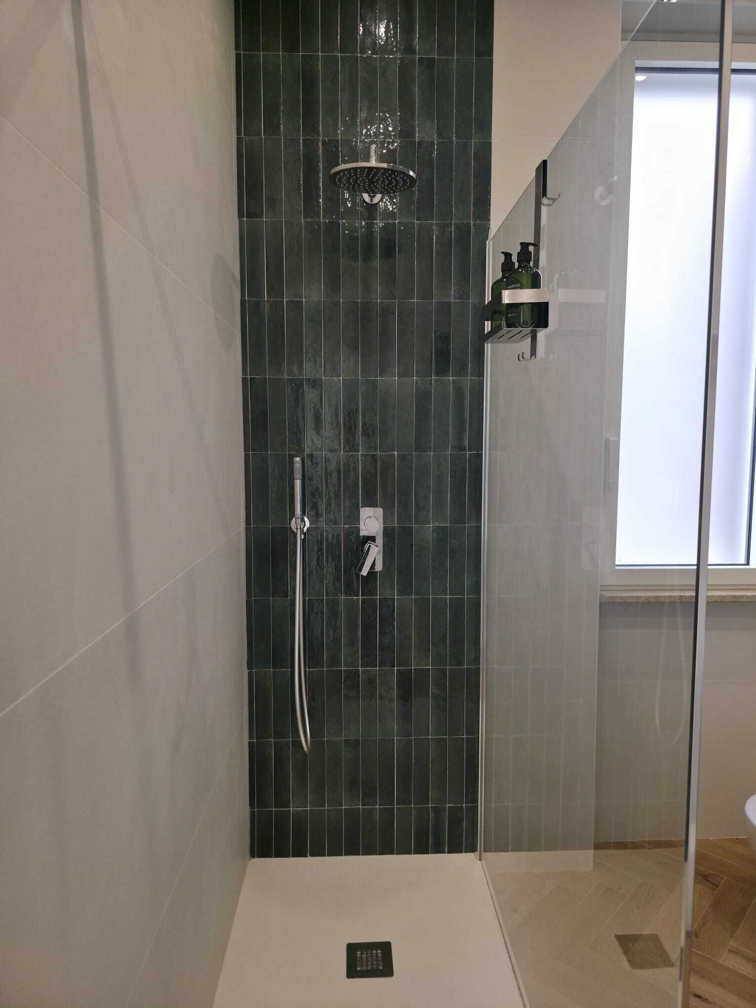A shower with a dark tiled wall, a handheld showerhead, and a handheld shower attachment.