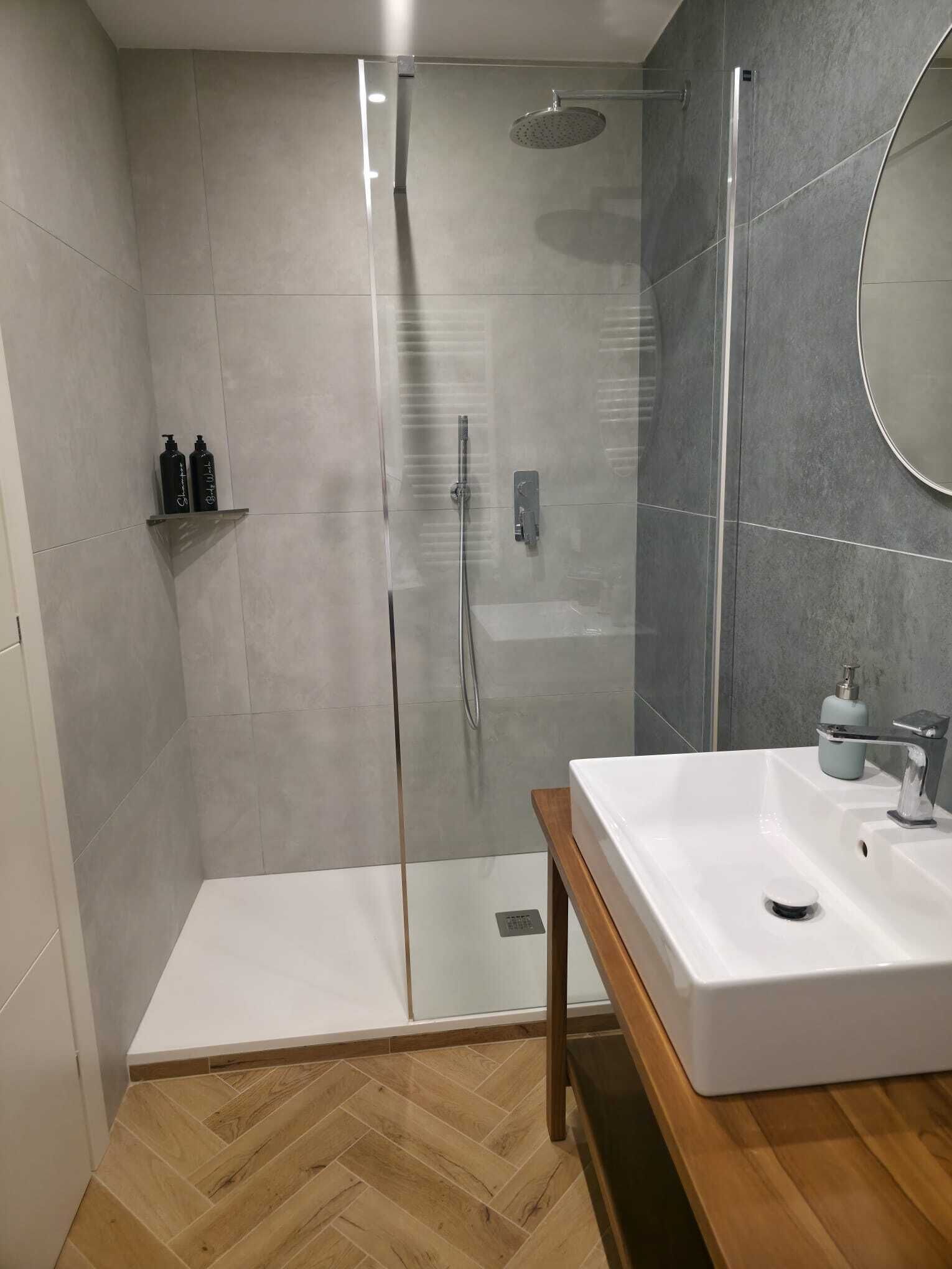 Un baño moderno con ducha envuelta en vidrio, un lavamanos blanco y suelo de madera.