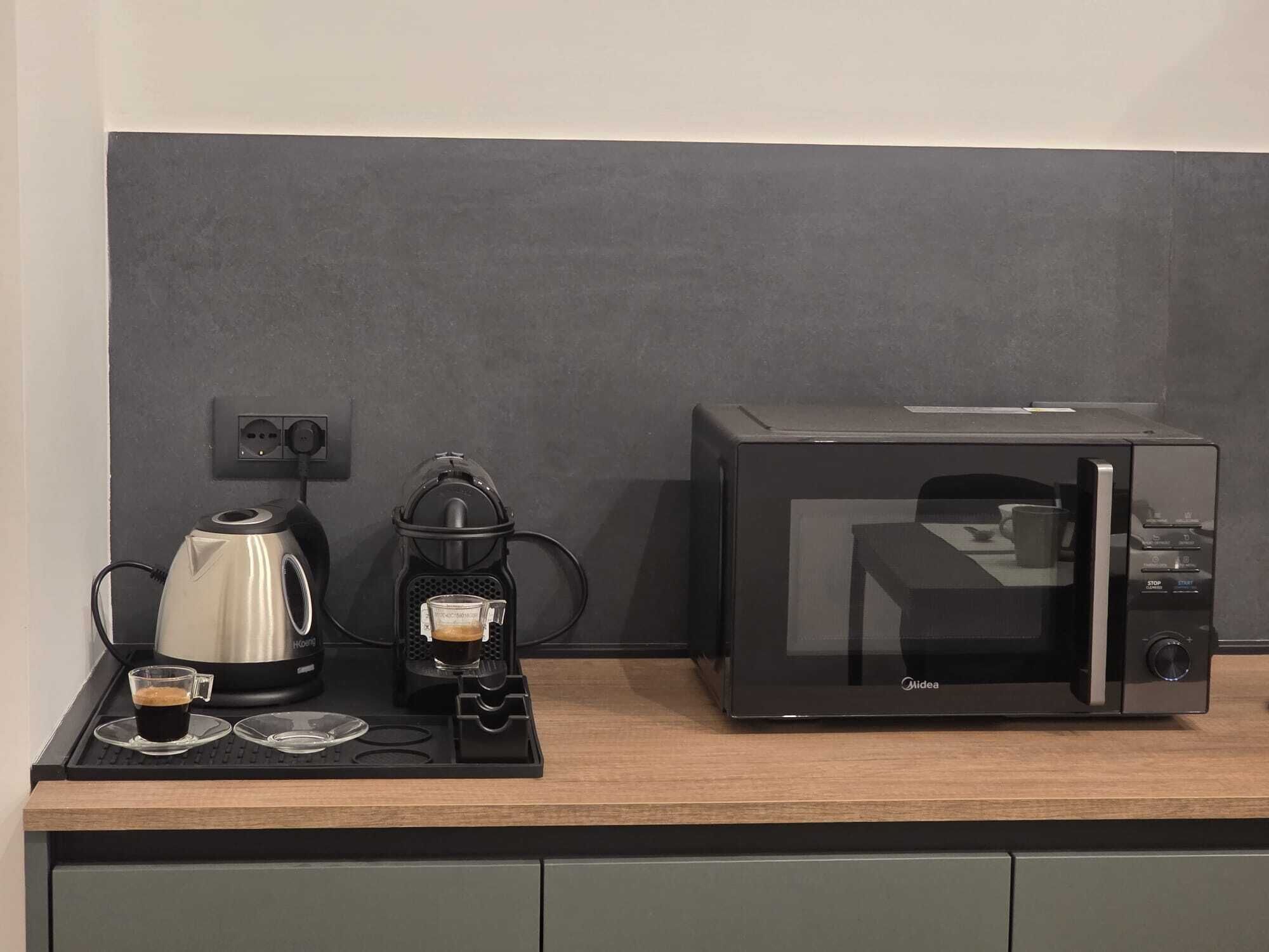 Una kitchenette con cafetera, una taza de café y un microondas sobre una encimera de madera.