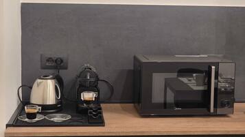 Una kitchenette con cafetera, una taza de café y un microondas sobre una encimera de madera.