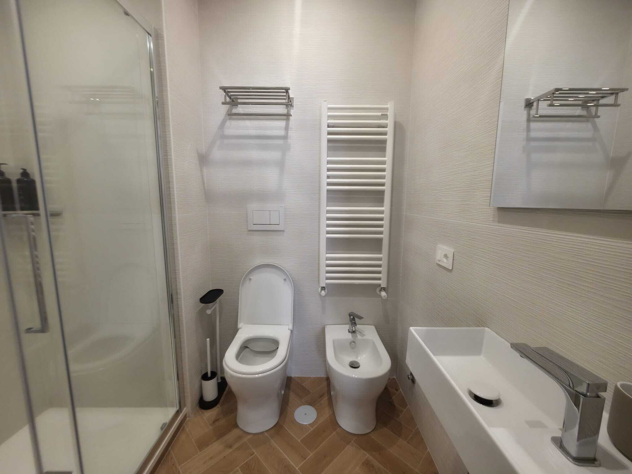 A modern bathroom with a glass shower enclosure, a toilet, a bidet, and a bathtub.