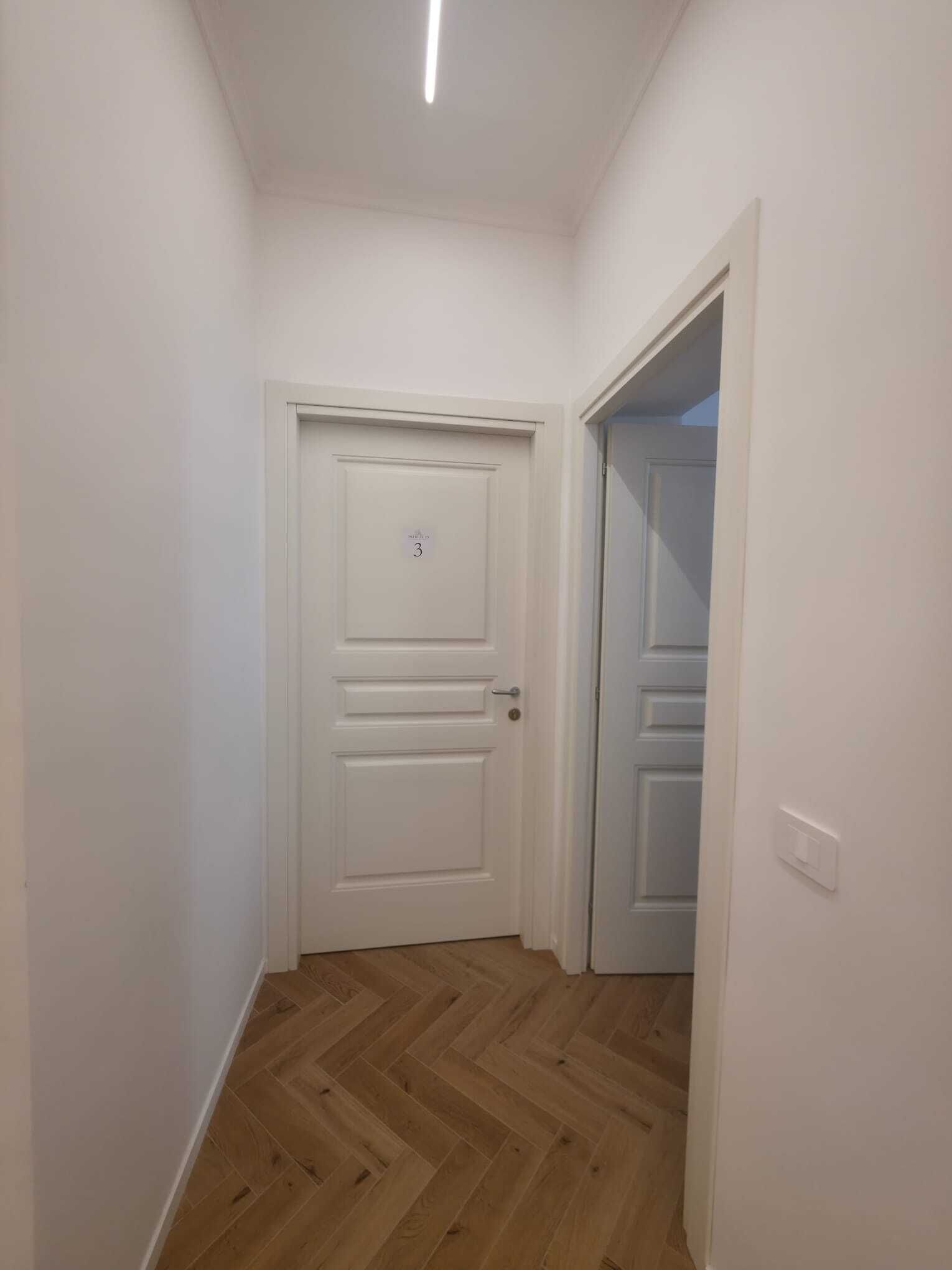 A hallway with a white door marked with the number 3, wooden flooring, and a light switch on the wall.