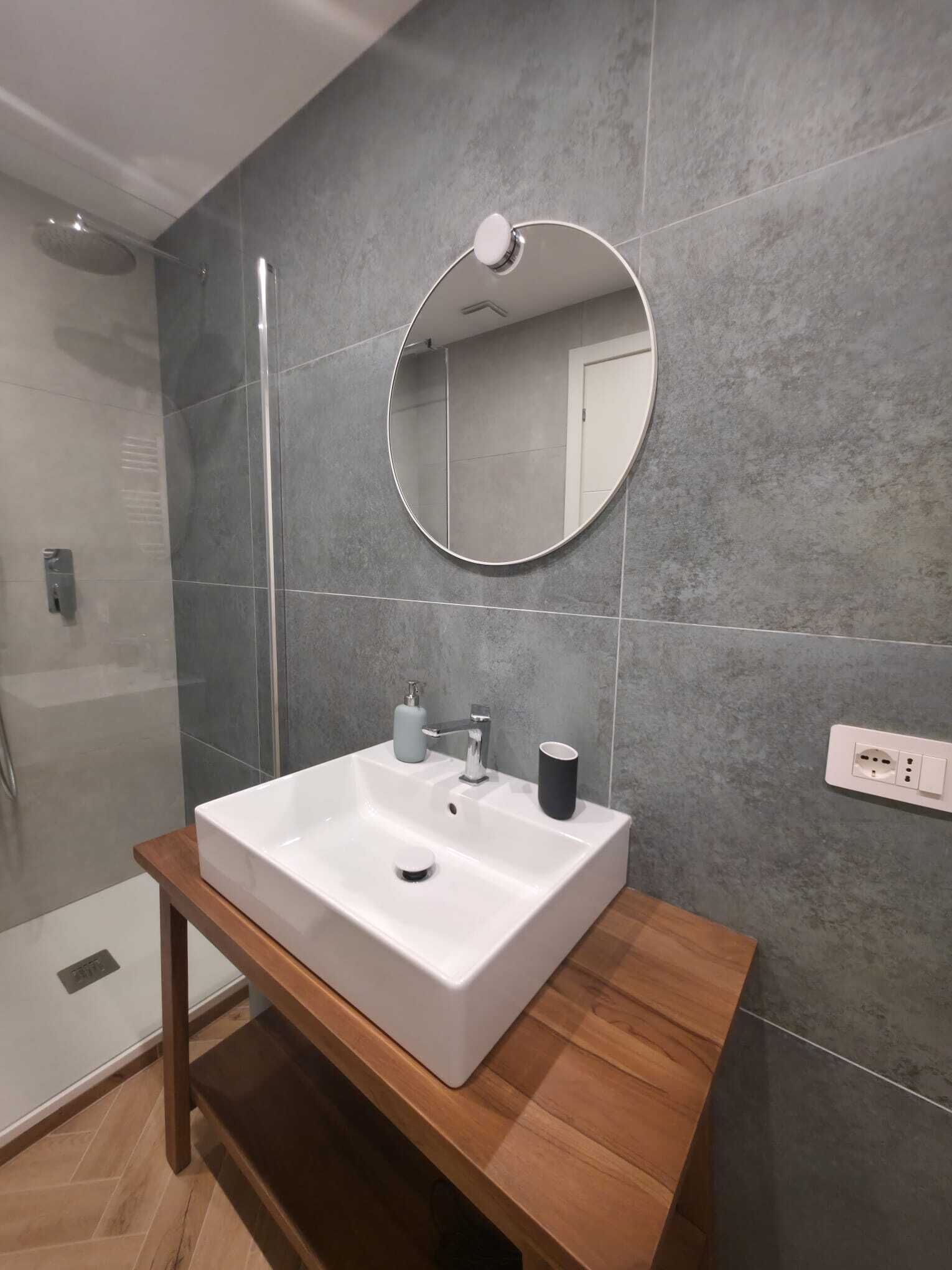 A modern bathroom with a rectangular sink, a round mirror, and a shower enclosure.