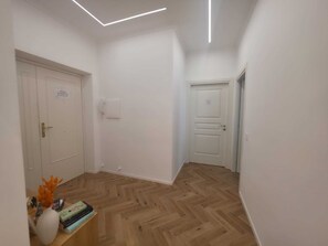 A hallway with wooden flooring, white walls, and doors. There is a small shelf with books and a vase with flowers. - Domus 39 by Be Your Home (Civitavecchia)