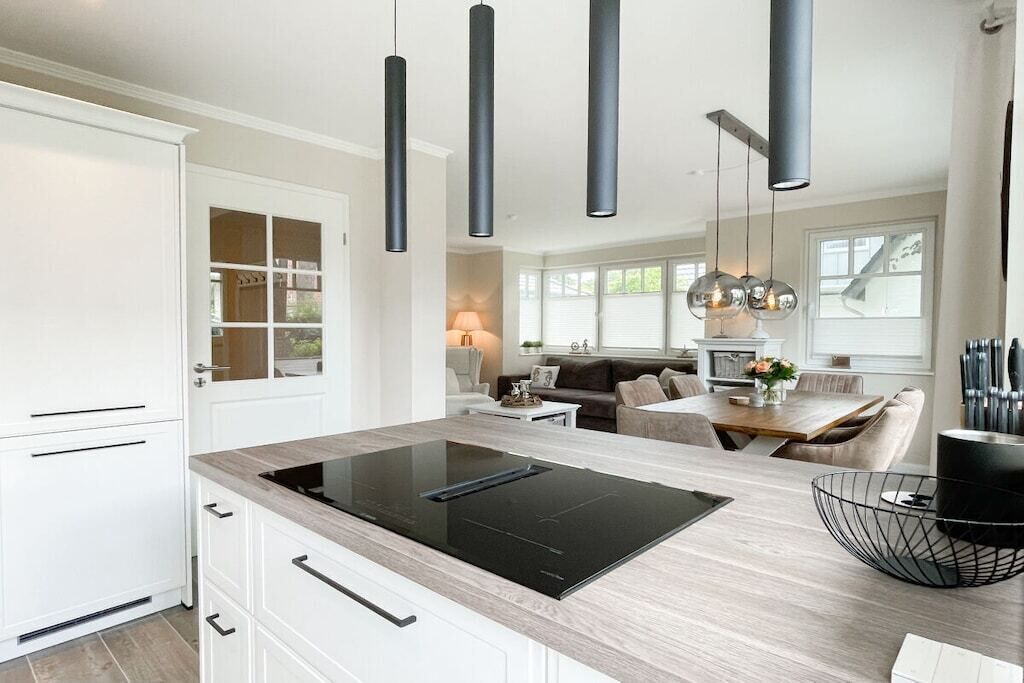 A modern kitchen with a central island, pendant lighting, and a dining area with a table and chairs.