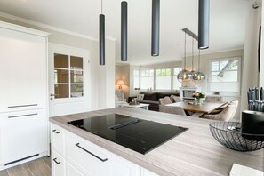 A modern kitchen with a central island, pendant lighting, and a dining area with a table and chairs. - Holiday home with 3 bedrooms (Timmendorfer Strand)