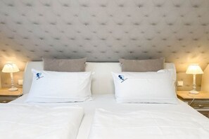 Ein Hotelzimmer mit einem karrenförmigen Kopfteil, zwei Betten mit weißen Leinentüchern und zwei Nachttischlampen.