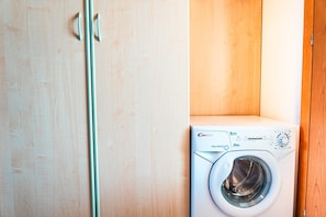 A front-loading washing machine in a laundry room with wooden cabinets. - Cozy flat with pool access (Bibione)