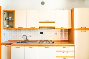 A kitchen with white cabinets, a gas stove, a sink, and a window vent. - Cozy flat with pool access (Bibione)