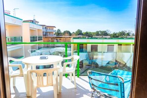 A balcony with a table and chairs, a pool, and a view of surrounding buildings. - Cozy flat with pool access (Bibione)