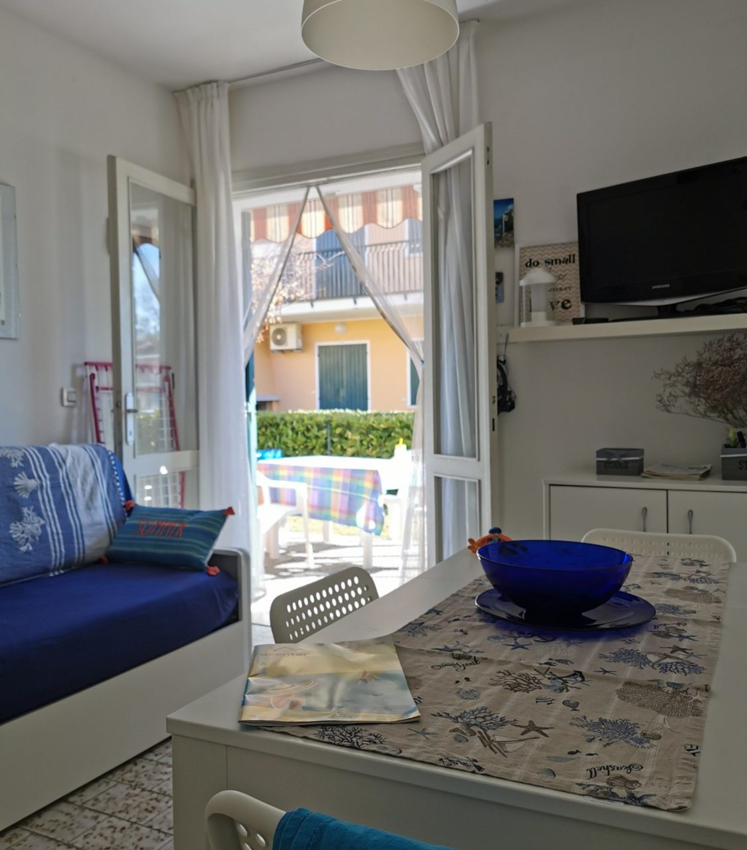 A room with a sofa, a table with a bowl, a television, and a view of the outside balcony.