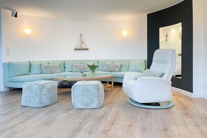 Ein modernes Wohnzimmer mit einem hellblauen Sofa, einem weißen Sessel und zwei Poufs.