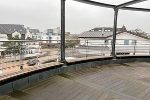 Ein überdachter Außenbereich mit Metallgeländer, einer Holzterrasse und Blick auf Wohnhäuser.