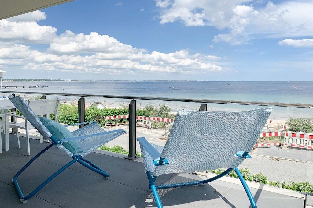 Two mesh lounge chairs on an outdoor balcony with a view of the sea.