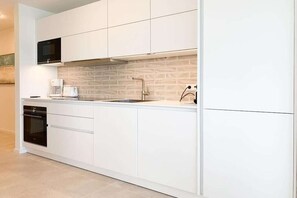 A modern kitchen with white cabinetry, a built-in oven, a coffee maker, and a brick backsplash. - House on the beach, Apartment 7 (Scharbeutz)