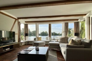 A spacious living room with a large TV, comfortable seating, and a view of a lake. - Landhaus Lotten - Exclusive (Winsen)