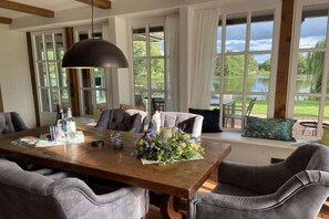 Un coin repas avec une table en bois, des chaises à revêtement gris et une grande fenêtre donnant sur un paysage verdoyant.
