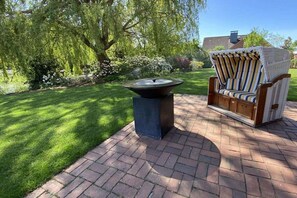A patio with a fire pit, a wicker chair, and a lush garden. - Landhaus Lotten - Exclusive (Winsen)