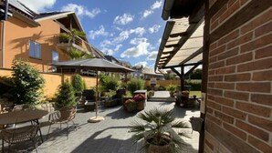 Ein Terrassenbereich im Freien mit Tischen, Stühlen, Topfpflanzen und einer überdachten Sitzgelegenheit.