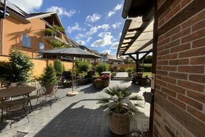Ein Terrassenbereich im Freien mit Tischen, Stühlen, Topfpflanzen und einer überdachten Sitzgelegenheit.