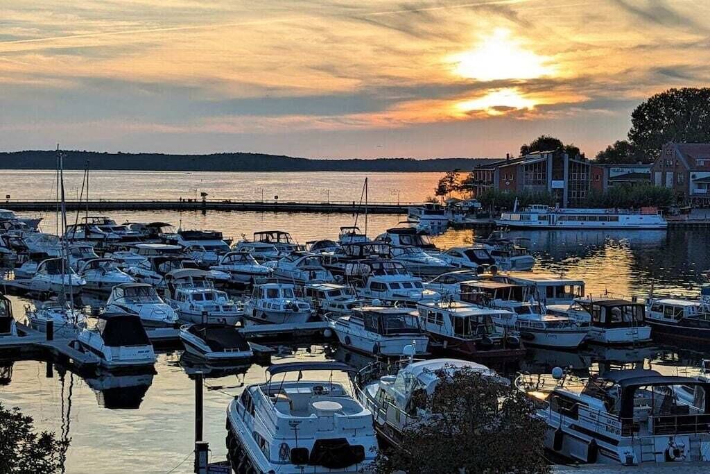 A marina with numerous boats docked, a calm water body, and buildings in the background.