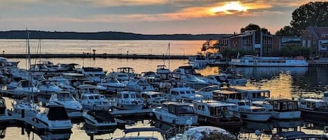 A marina with numerous boats docked, a calm water body, and buildings in the background.