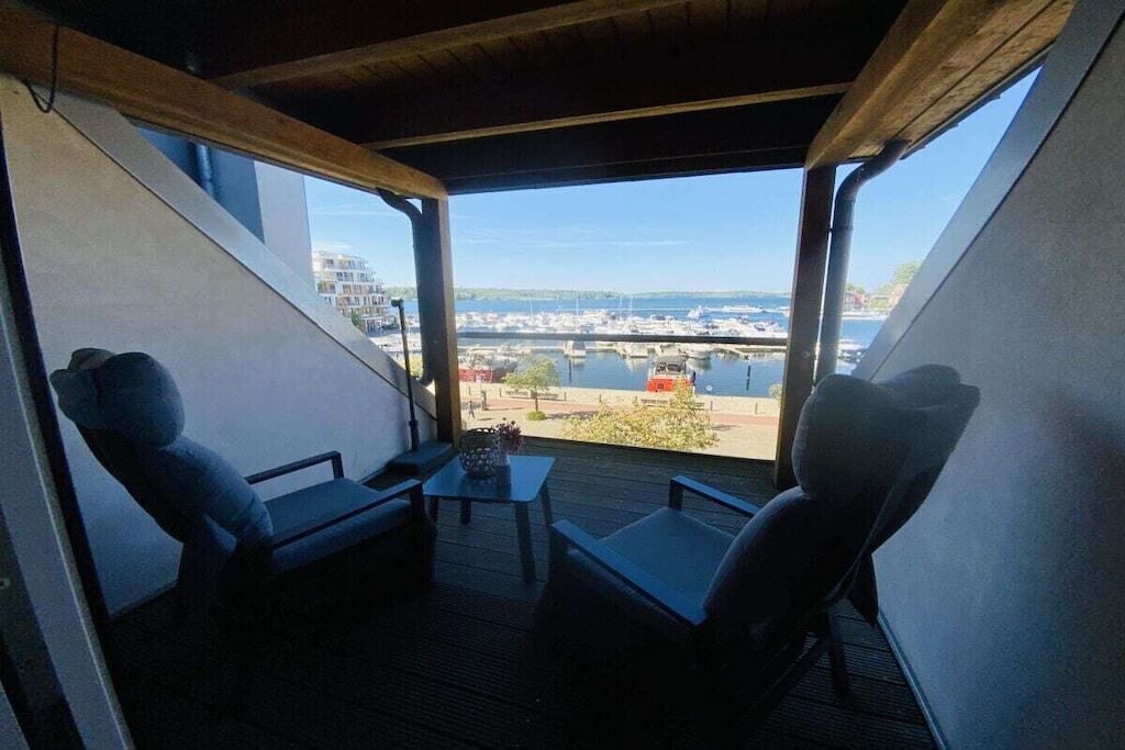A balcony with a view of a marina and buildings. There are two chairs and a small table.